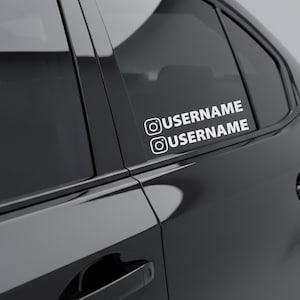 Könnte beinhalten: Ein weißer Vinyl-Aufkleber auf der hinteren Beifahrerseite eines schwarzen Autos. Der Aufkleber zeigt zwei Textzeilen, jeweils mit dem Instagram-Kamerasymbol davor, und dem Wort USERNAME in einer fetten, serifenlosen Großbuchstabenschrift.