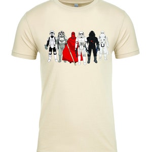 Puede incluir: Una camiseta de color crema con un gr&aacute;fico de seis personajes de Star Wars. Los personajes llevan todos atuendos diferentes y est&aacute;n en fila. Los personajes son, de izquierda a derecha: un Stormtrooper, un Rebel Trooper, un Guardia Real, un Stormtrooper, un Darth Vader y un Stormtrooper.