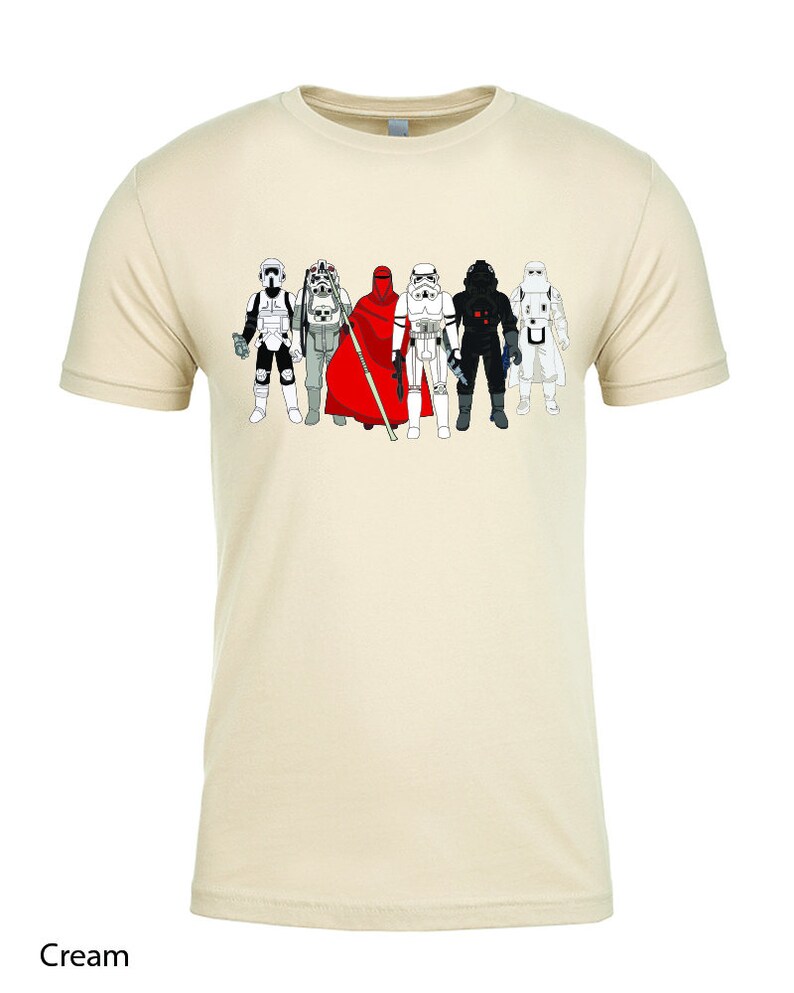 Puede incluir: Una camiseta de color crema con un gr&aacute;fico de seis personajes de Star Wars. Los personajes llevan todos atuendos diferentes y est&aacute;n en fila. Los personajes son, de izquierda a derecha: un Stormtrooper, un Rebel Trooper, un Guardia Real, un Stormtrooper, un Darth Vader y un Stormtrooper.