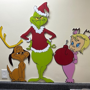 May include: Grinch, Max the dog, and Cindy Lou Who from the classic Christmas movie 'How the Grinch Stole Christmas'. The Grinch is wearing a red and white Santa suit, Max is wearing a red collar, and Cindy Lou Who is wearing a pink dress and holding a red ornament.