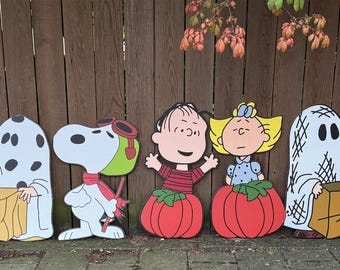 May include: A set of seven Peanuts character yard decorations featuring Lucy as a witch, a ghost, Snoopy as a pilot, Charlie Brown, Sally, another ghost, and a green-faced figure, all dressed in Halloween costumes and holding treat bags.