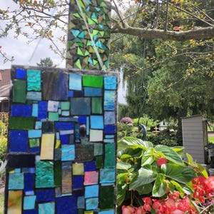 May include: A colorful mosaic glass suncatcher with blue, green, and yellow squares. The suncatcher is hanging from a tree branch.