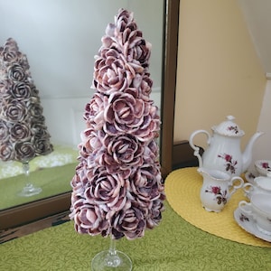 May include: A purple and white seashell Christmas tree decoration. The tree is made of many small seashells that are arranged in a spiral pattern. The tree is on a clear glass stand.