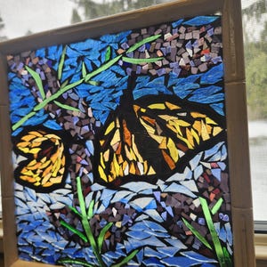 May include: A mosaic artwork featuring two butterflies with yellow and orange wings, set against a blue and purple background. Green stems and leaves are also included. The artwork is framed in a light brown bamboo-style frame.