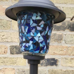 May include: A blue mosaic glass lamp post with a black metal top and base. The mosaic is made of small, irregular pieces of glass in shades of blue, white, and black.