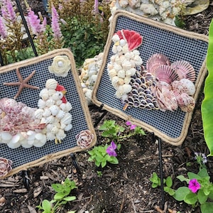 May include: Two framed wall art pieces made of seashells, each depicting a rooster. The rooster on the left is white and the rooster on the right is red, white, and purple.