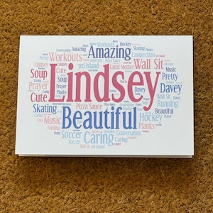 May include: A white card with the name "Lindsey" in pink and a collection of related words in blue and pink. Words include "Beautiful", "Cute", "Soccer", and "Prayer". The card is on a brown surface.