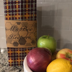May include: A set of three reusable food wraps with a plaid pattern in shades of yellow, red, and blue. The wraps are made by All's Bee Keepers and are labeled as sustainable, reusable, and eco-friendly.