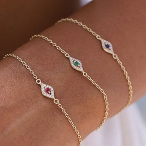 May include: Three gold chain bracelets with a diamond-encrusted evil eye charm. Each charm features a different colored gemstone in the center: red, green, and blue.