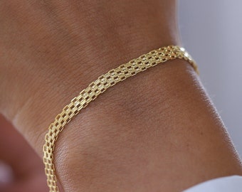May include: A gold chain bracelet with a delicate, woven design. The bracelet is worn on a person's wrist.