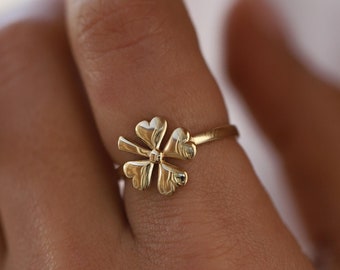 Puede incluir: Un anillo de oro con un diseño de trébol de cuatro hojas. El anillo se lleva en un dedo.