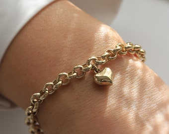 Peut inclure: Un bracelet en chaîne dorée avec un pendentif en forme de cœur. Le bracelet est porté au poignet.