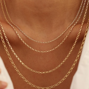May include: Four gold chain necklaces layered on a person's neck. The chains are of different lengths and thicknesses.