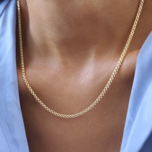 Puede incluir: Un collar de cadena de oro con un diseño delicado e entrelazado. La cadena la lleva puesta una persona con una camisa azul.