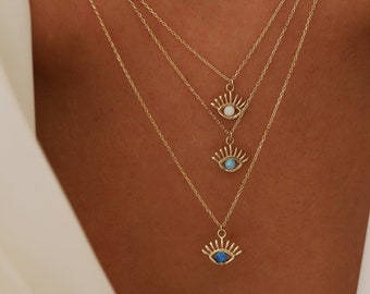 May include: Three gold necklaces with evil eye pendants. The pendants are adorned with blue and white opal stones.