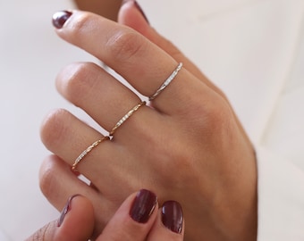 Könnte beinhalten: Drei zarte goldene Ringe mit kleinen Diamanten, die in einem gedrehten Band gefasst sind.