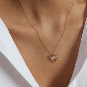 May include: A gold-colored necklace with a heart-shaped pendant. The pendant features a musical note design in a contrasting silver color. The necklace is worn against a white shirt.