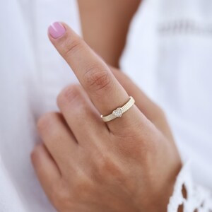 K&ouml;nnte beinhalten: Ein goldener Ring mit einem kleinen herzf&ouml;rmigen Diamanten in der Mitte. Der Ring befindet sich an einem Finger.