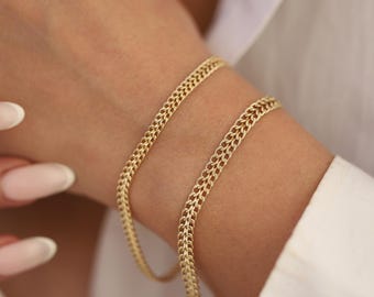 May include: Two gold chain bracelets on a person's wrist. The bracelets are made of a thick, textured chain.