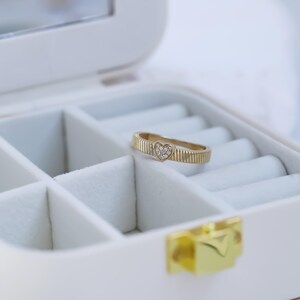 K&ouml;nnte beinhalten: Ein goldener Ring mit einem kleinen herzf&ouml;rmigen Diamanten in der Mitte. Der Ring liegt in einer wei&szlig;en Ringbox.