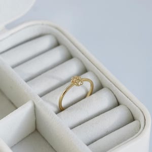 May include: A gold ring with a textured flower design. The ring is sitting in a white ring box.