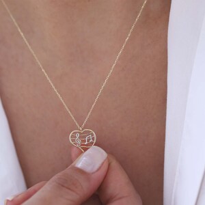 May include: A gold-colored necklace with a heart-shaped pendant. The pendant features a musical note design with a treble clef and a quarter note. The necklace is worn around the neck.