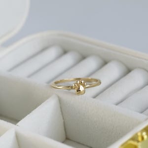 May include: A gold ring with a paw print design. The ring is sitting in a white ring box.