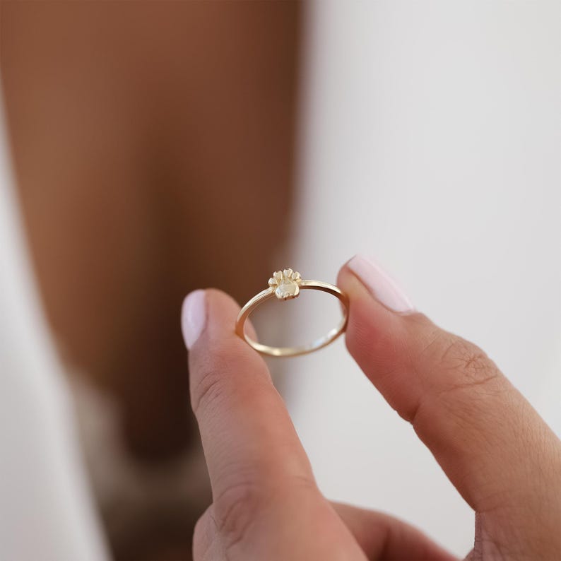 May include: A delicate gold ring with a small, flower-shaped design in the center.