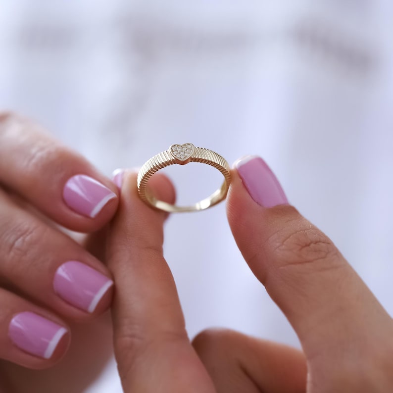 K&ouml;nnte beinhalten: Ein goldener Ring mit einem herzf&ouml;rmigen Diamanten in der Mitte. Der Ring hat eine strukturierte Band.