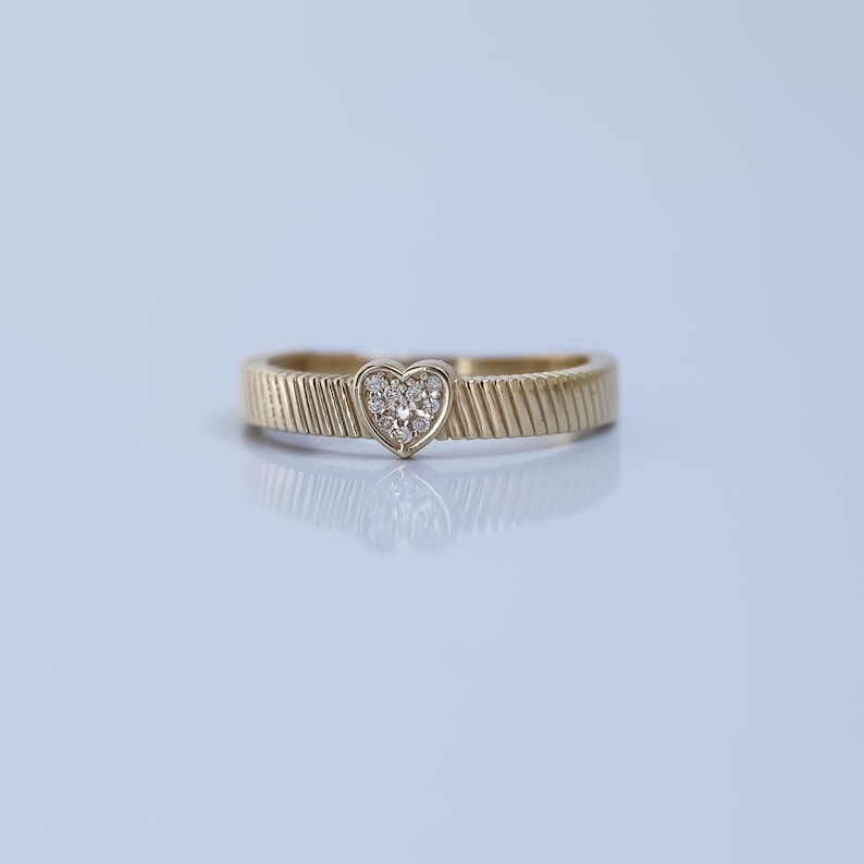 K&ouml;nnte beinhalten: Ein Goldring mit einem herzf&ouml;rmigen Diamantenbesatz. Die Band hat ein strukturiertes Design.