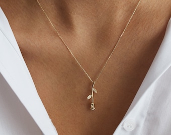May include: A delicate gold necklace with a rose pendant. The rose is stylized with a single stem and leaves.
