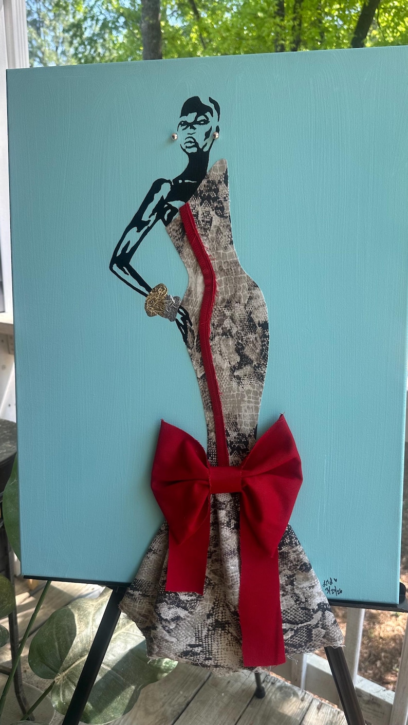 Puede incluir: Obra de arte en lienzo que presenta una silueta estilizada de una persona con un vestido con estampado de piel de serpiente y un gran lazo rojo. La figura tiene brazos negros y cabeza negra. Una raya roja recorre el centro del vestido. El fondo es azul claro.