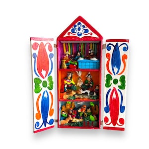 May include: A colorful wooden nativity scene with a red roof and painted details. The scene features a family of figures dressed in traditional clothing, with a manger and animals.