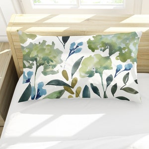 May include: Two white pillowcases with a green and blue watercolor floral pattern. The pillowcases are on a white bed with a white headboard.