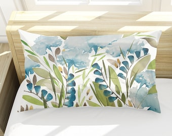 May include: Two white pillowcases with a blue and green watercolor floral pattern. The pillowcases are on a white bed with a wooden headboard.