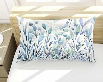 May include: Two white pillowcases with a blue and green watercolor floral pattern. The pillowcases are on a white bed with a wooden headboard.