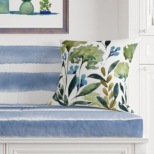 May include: A white bench with blue and white striped cushions and a green floral pillow. A framed watercolor painting of potted plants hangs above the bench.