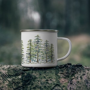 May include: White enamel mug with a watercolor design of a forest of green trees. The mug has a silver rim and handle.