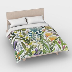 K&ouml;nnte beinhalten: Ein wei&szlig;er Bettbezug mit einem Blumenmuster aus gr&uuml;nen Bl&auml;ttern, gelben, orangefarbenen, blauen und violetten Blumen.