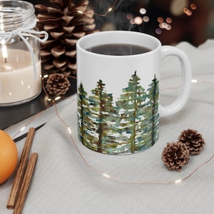 May include: White ceramic mug with a watercolor design of a forest scene. The mug is filled with coffee and has a brown handle.