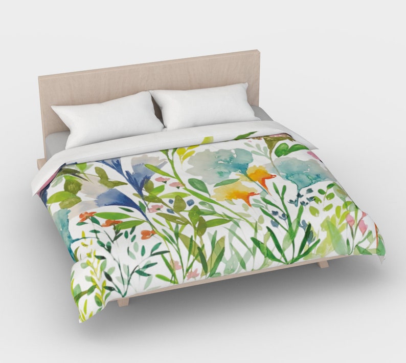 May include: A white duvet cover with a watercolor floral pattern featuring blue, green, yellow, and orange flowers. The duvet cover is on a bed with a wooden headboard and two white pillows.