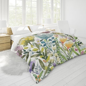 K&ouml;nnte beinhalten: Ein wei&szlig;er Bettbezug mit einem Aquarell-Blumenmuster mit gr&uuml;nen Bl&auml;ttern, gelben, blauen und rosa Bl&uuml;ten.