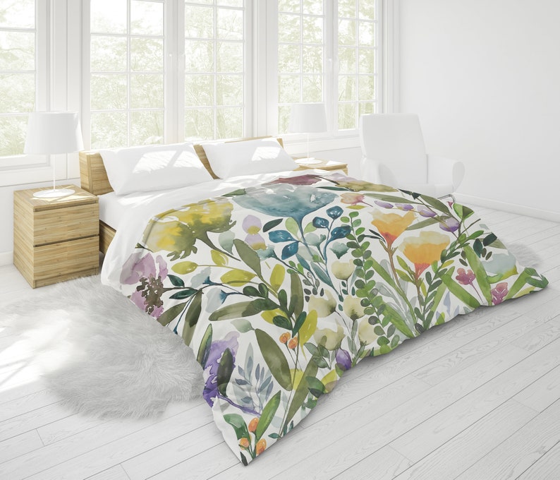 K&ouml;nnte beinhalten: Ein wei&szlig;er Bettbezug mit einem Aquarell-Blumenmuster mit gr&uuml;nen Bl&auml;ttern, gelben, blauen und rosa Bl&uuml;ten.