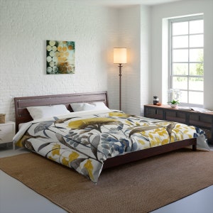 Pode incluir: Uma capa de edredom branca com um padrão floral de aquarela em tons de amarelo, azul e marrom. A capa de edredom está em uma cama com uma cabeceira de madeira e um tapete marrom.