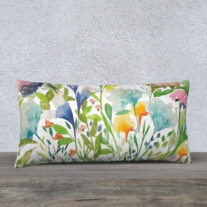 May include: A rectangular lumbar pillow with a watercolor floral print featuring blue, yellow, green, and pink flowers on a white background.