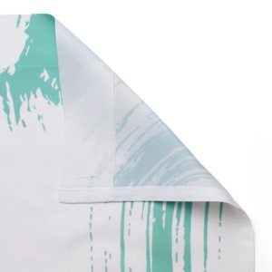 May include: Close-up of a white fabric with a green abstract pattern. The fabric is folded over, showing the reverse side.