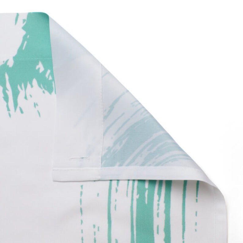May include: Close-up of a white fabric with a green abstract pattern. The fabric is folded over, showing the reverse side.