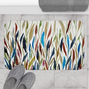 May include: A white bath mat with a colorful abstract design featuring blue, red, green, and yellow watercolor-like leaves. The design is reminiscent of a garden or forest.