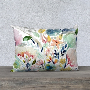 May include: A decorative throw pillow with a watercolor floral print featuring pink, yellow, blue, and green flowers on a white background.