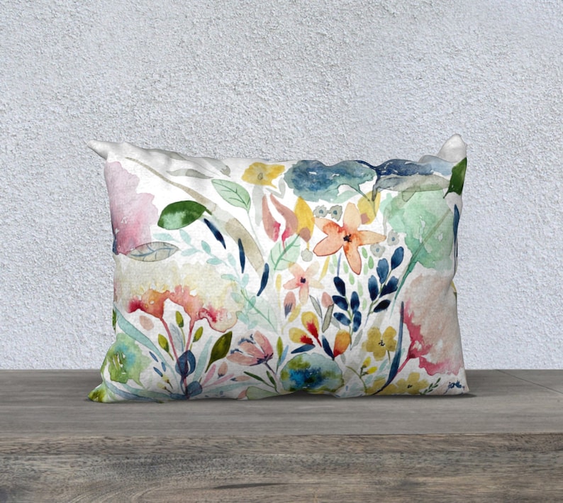 May include: A decorative throw pillow with a watercolor floral print featuring pink, yellow, blue, and green flowers on a white background.